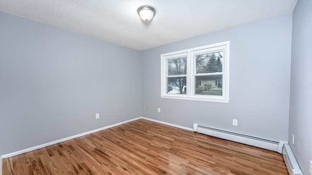 spare room with a textured ceiling, baseboard heating, wood finished floors, and baseboards