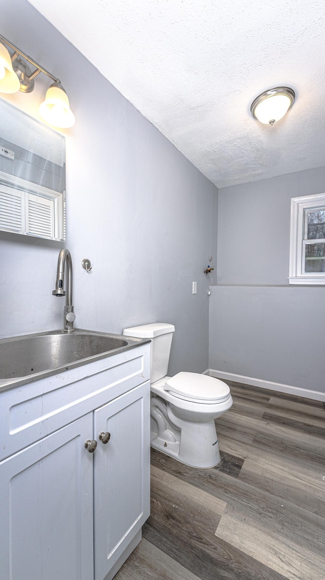 bathroom with a textured ceiling, toilet, wood finished floors, vanity, and baseboards