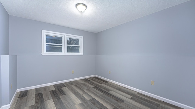 spare room featuring a textured ceiling, dark wood finished floors, and baseboards