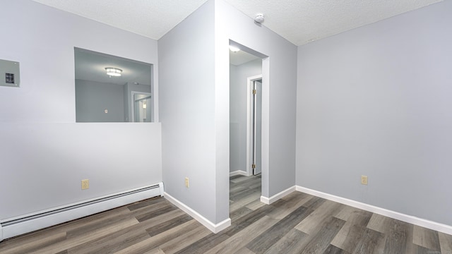 empty room featuring a textured ceiling, a baseboard radiator, wood finished floors, and baseboards