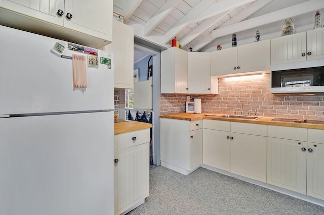 kitchen featuring lofted ceiling with beams, freestanding refrigerator, a sink, butcher block countertops, and black electric cooktop