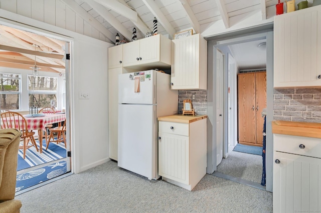 kitchen featuring butcher block counters, lofted ceiling with beams, freestanding refrigerator, light carpet, and white cabinetry