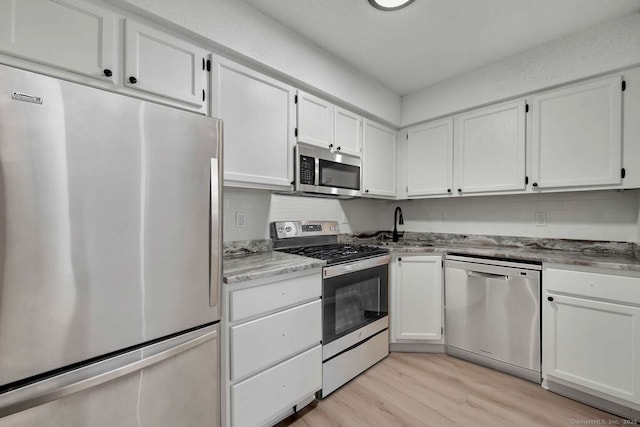 kitchen with light wood finished floors, appliances with stainless steel finishes, a sink, and white cabinetry