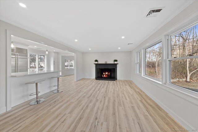 unfurnished living room featuring a warm lit fireplace, a wealth of natural light, visible vents, and baseboards