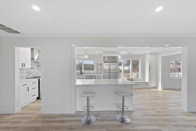 interior space with a kitchen bar, light countertops, appliances with stainless steel finishes, white cabinets, and wall chimney exhaust hood