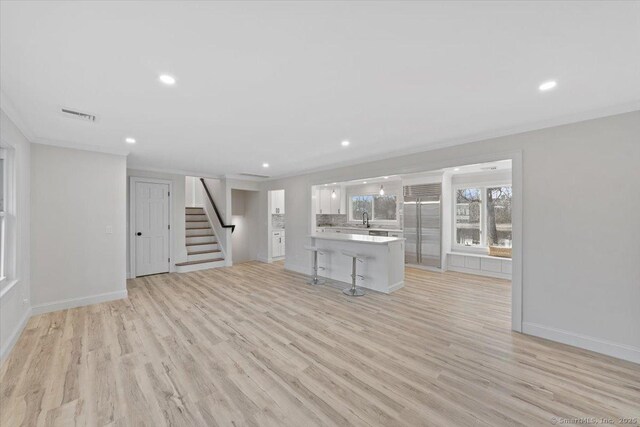 unfurnished living room featuring light wood-type flooring, visible vents, stairway, and ornamental molding