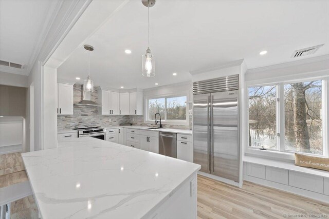 kitchen featuring ornamental molding, wall chimney exhaust hood, appliances with stainless steel finishes, and visible vents