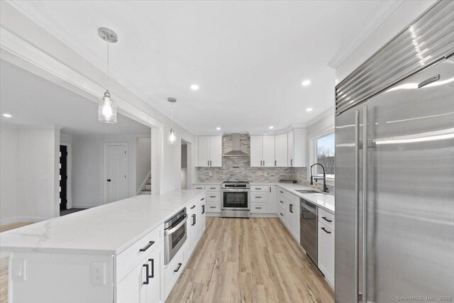 kitchen with a sink, ornamental molding, appliances with stainless steel finishes, decorative backsplash, and wall chimney exhaust hood