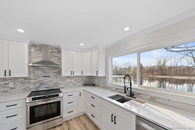 kitchen featuring light wood-style flooring, backsplash, stainless steel range with electric cooktop, a sink, and wall chimney range hood