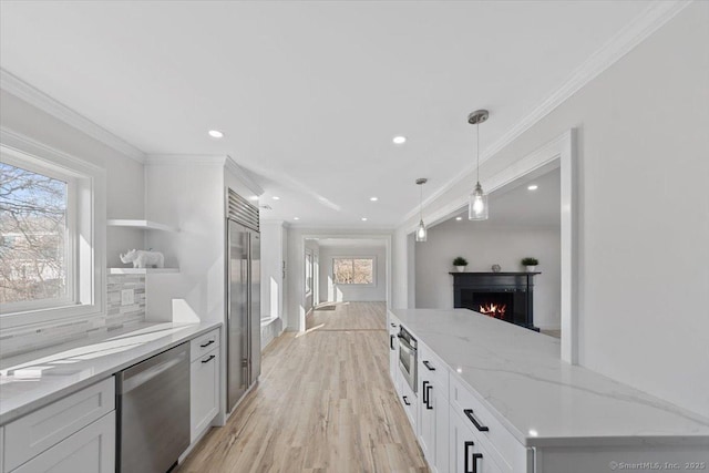 kitchen with crown molding, stainless steel appliances, decorative backsplash, white cabinets, and a warm lit fireplace