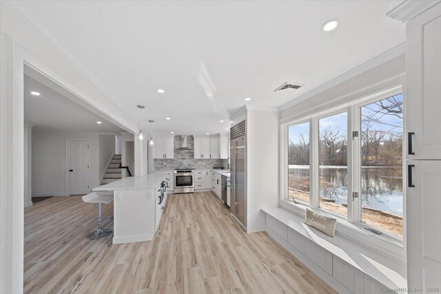 kitchen featuring wall chimney exhaust hood, ornamental molding, a breakfast bar, stainless steel appliances, and backsplash