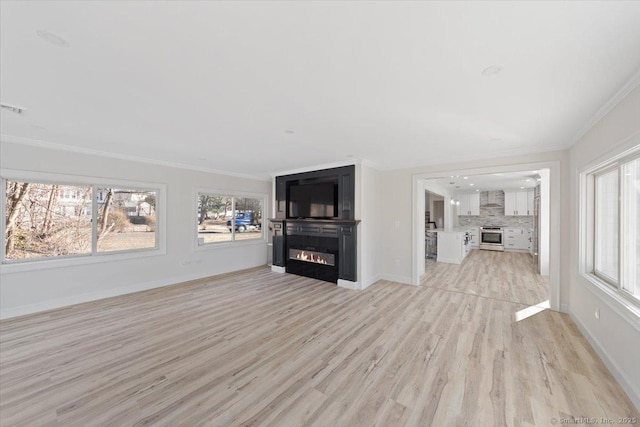 unfurnished living room featuring baseboards, light wood-style floors, a glass covered fireplace, and crown molding