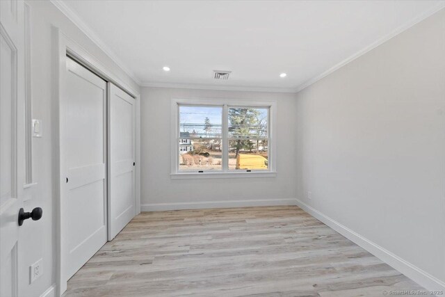 unfurnished bedroom with baseboards, visible vents, ornamental molding, light wood-type flooring, and a closet