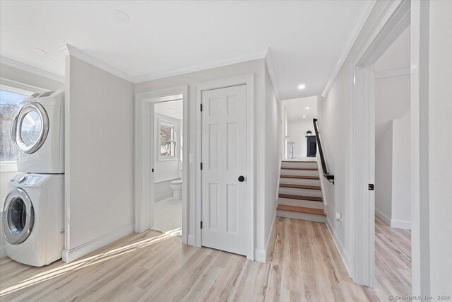 clothes washing area featuring stacked washer and dryer, laundry area, crown molding, and light wood-style flooring