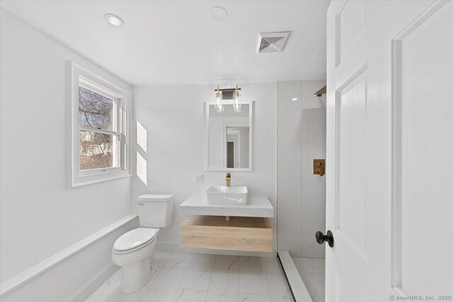 bathroom with toilet, visible vents, baseboards, marble finish floor, and tiled shower