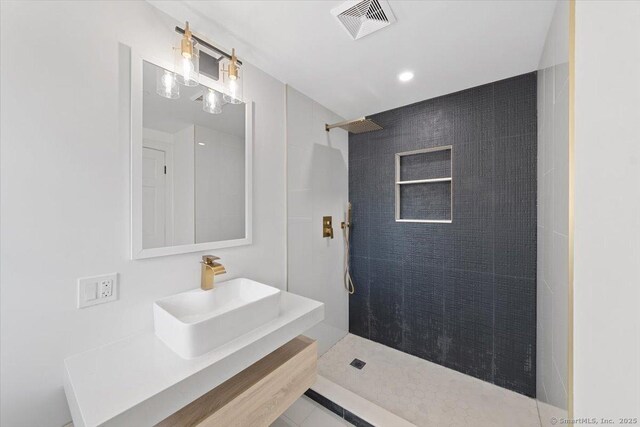 bathroom with tiled shower, a sink, and visible vents