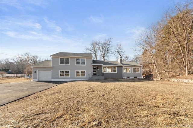 split level home featuring a garage, a chimney, aphalt driveway, and a front yard