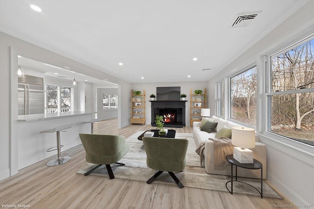 living area featuring a warm lit fireplace, a wealth of natural light, wood finished floors, and visible vents