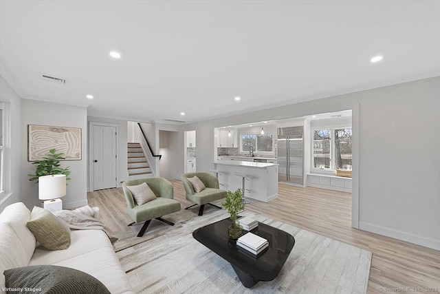 living area with baseboards, visible vents, stairs, light wood-type flooring, and recessed lighting