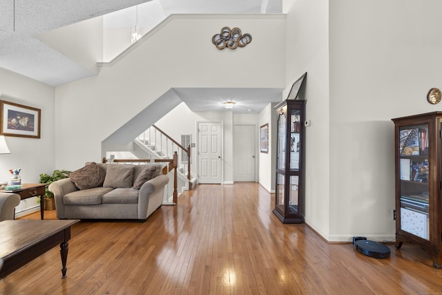 living area with high vaulted ceiling, stairway, hardwood / wood-style flooring, and baseboards