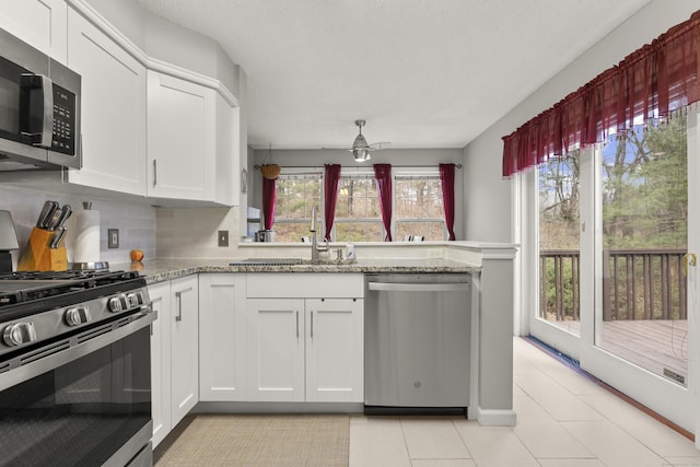 kitchen featuring a peninsula, light stone countertops, stainless steel appliances, white cabinetry, and a sink