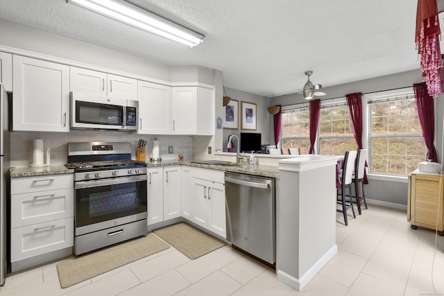 kitchen featuring white cabinets, appliances with stainless steel finishes, a peninsula, light stone countertops, and a sink