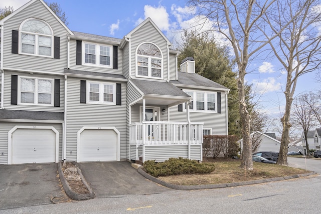 view of front of house with an attached garage, driveway, a chimney, and a porch