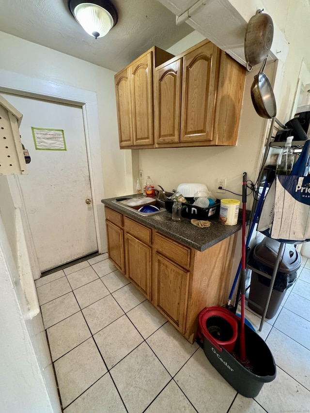 kitchen featuring dark countertops, light tile patterned floors, brown cabinets, and a sink