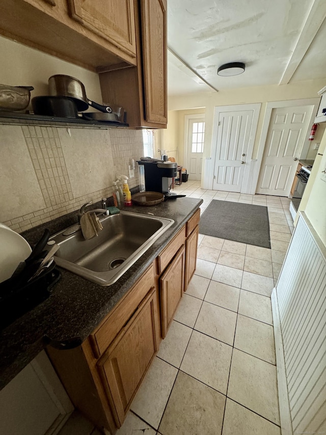 kitchen featuring light tile patterned floors, tasteful backsplash, dark countertops, stove, and a sink