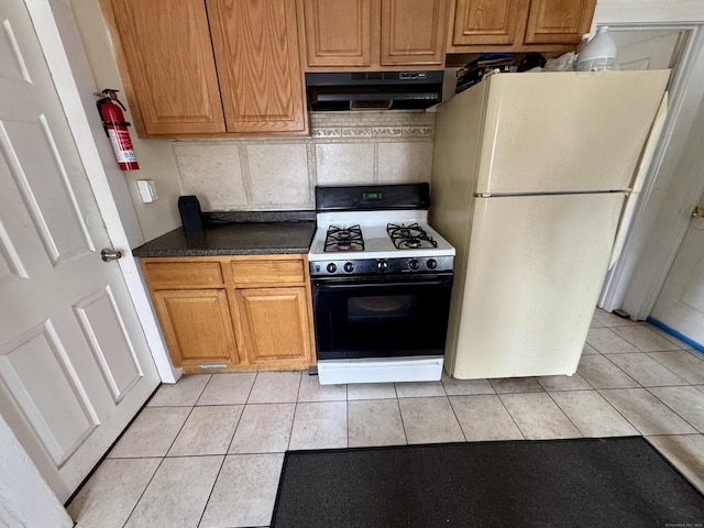 kitchen with light tile patterned floors, range with gas stovetop, dark countertops, freestanding refrigerator, and under cabinet range hood