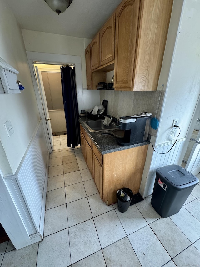 kitchen featuring light tile patterned flooring, a sink, backsplash, brown cabinets, and dark countertops