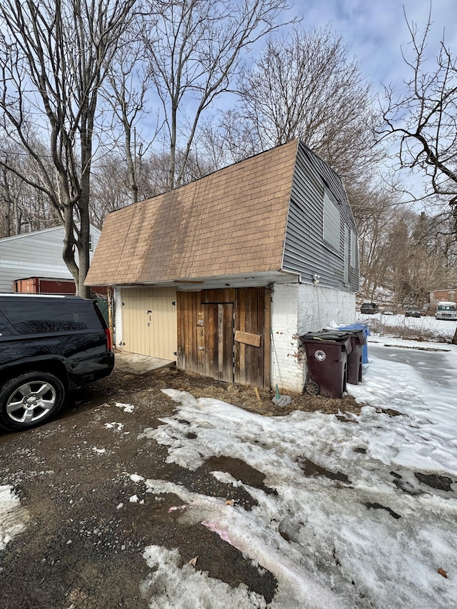 view of snow covered exterior with a shingled roof, an outdoor structure, and a gambrel roof