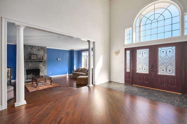 entryway with decorative columns, a high ceiling, a fireplace, and wood finished floors