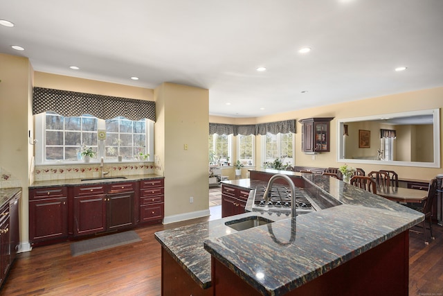 kitchen featuring reddish brown cabinets, dark wood-style floors, a sink, and an island with sink