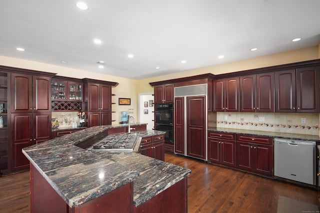 kitchen with dark wood-type flooring, a sink, appliances with stainless steel finishes, reddish brown cabinets, and an island with sink