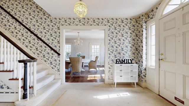 entryway with a notable chandelier, crown molding, wallpapered walls, baseboard heating, and stairs