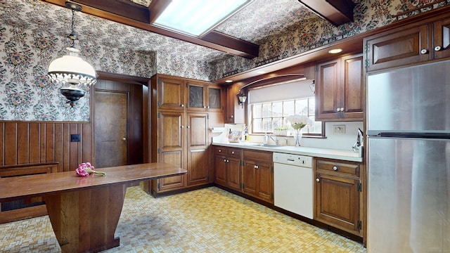 kitchen featuring a wainscoted wall, wallpapered walls, freestanding refrigerator, light countertops, and dishwasher