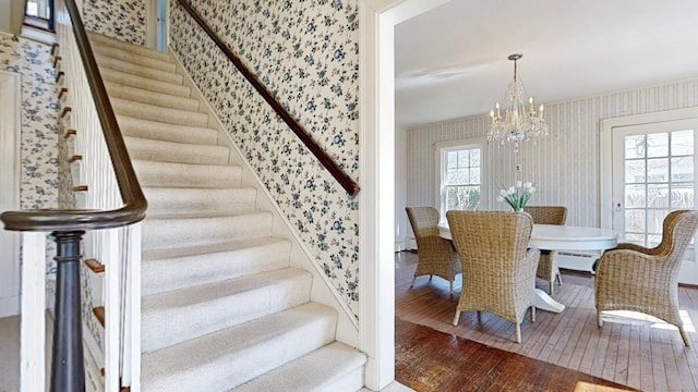 stairs with a chandelier, a healthy amount of sunlight, wallpapered walls, and hardwood / wood-style floors