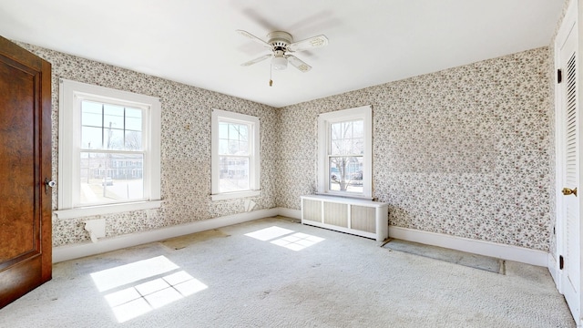 carpeted spare room with baseboards, radiator, ceiling fan, and wallpapered walls