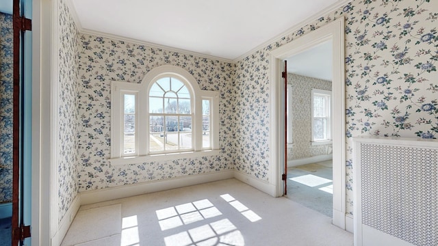 empty room featuring radiator, wallpapered walls, crown molding, baseboards, and carpet floors