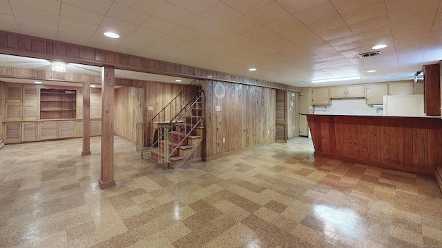 finished below grade area with visible vents, stairway, wood walls, and freestanding refrigerator