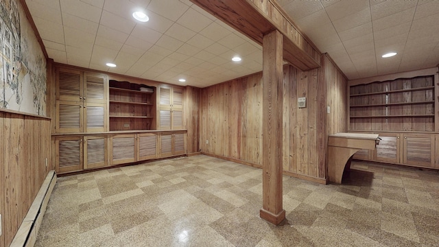 basement with wooden walls, built in shelves, built in study area, a baseboard radiator, and recessed lighting