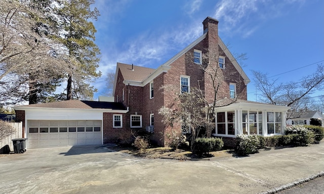 view of home's exterior featuring driveway, an attached garage, a sunroom, a chimney, and brick siding