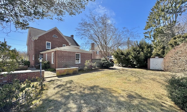 view of side of property with a storage unit, an outbuilding, a yard, brick siding, and a chimney