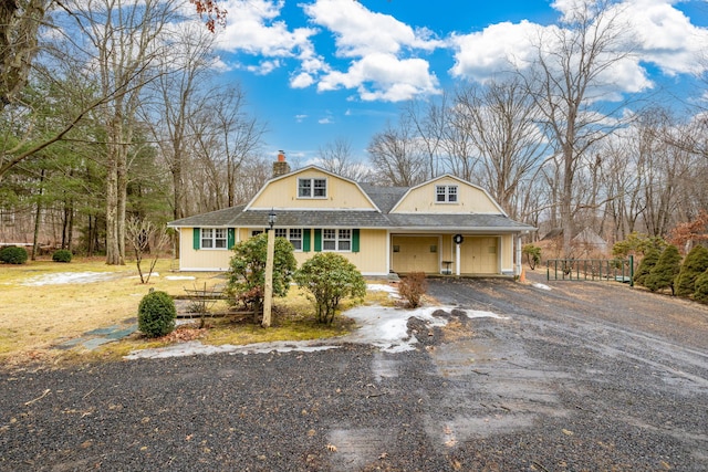 view of front facade featuring roof with shingles, a chimney, a gambrel roof, a garage, and driveway