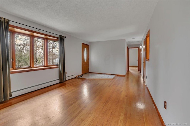 empty room featuring a baseboard heating unit, light wood-type flooring, a textured ceiling, and baseboards