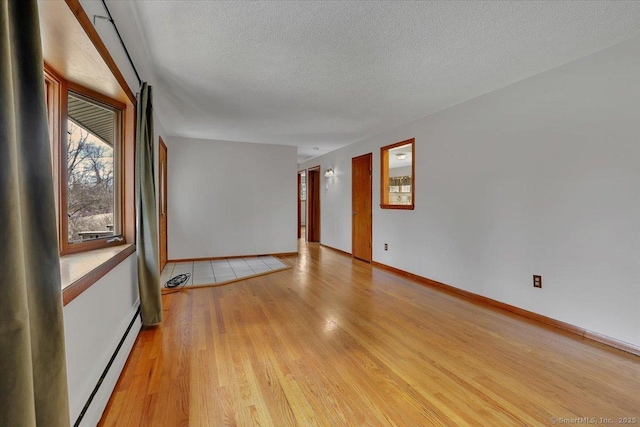 empty room featuring light wood-style floors, baseboards, a textured ceiling, and baseboard heating