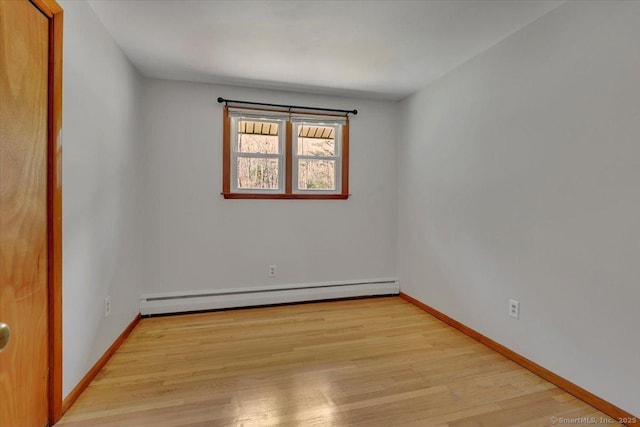 spare room featuring a baseboard heating unit, light wood-style flooring, and baseboards