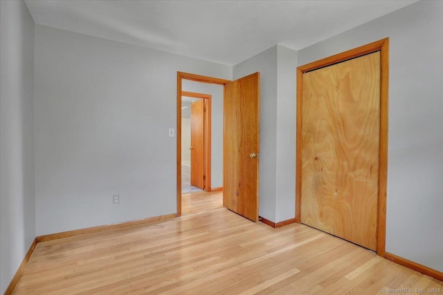 unfurnished bedroom with light wood-type flooring, a closet, and baseboards