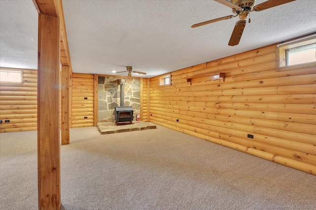 basement with a wood stove, a ceiling fan, a textured ceiling, and carpet flooring